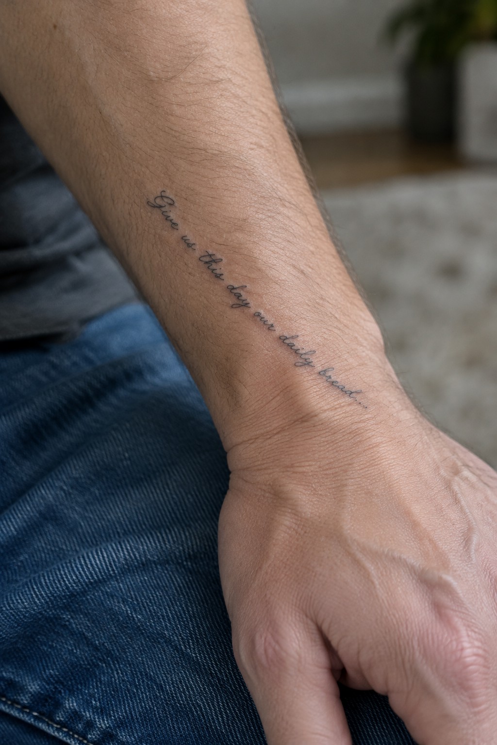 Inner forearm tattoo with the bible verse give us this day our daily bread written in thin cursive script