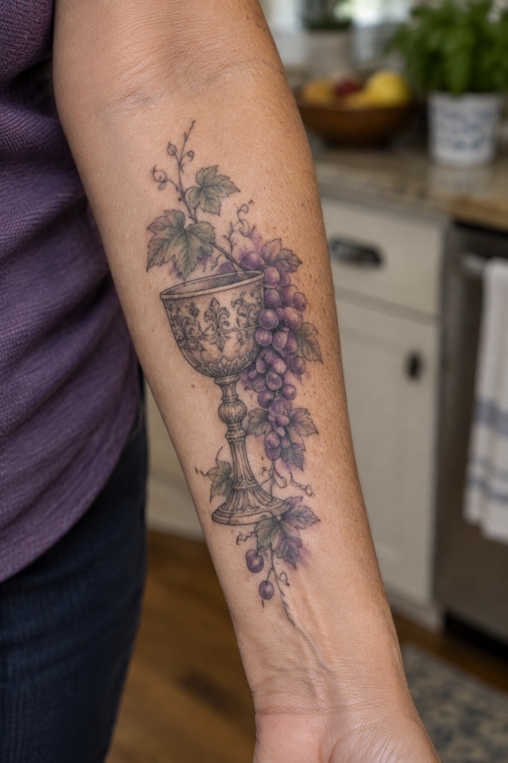 Ornate chalice tattoo with purple grapes and green vines on forearm