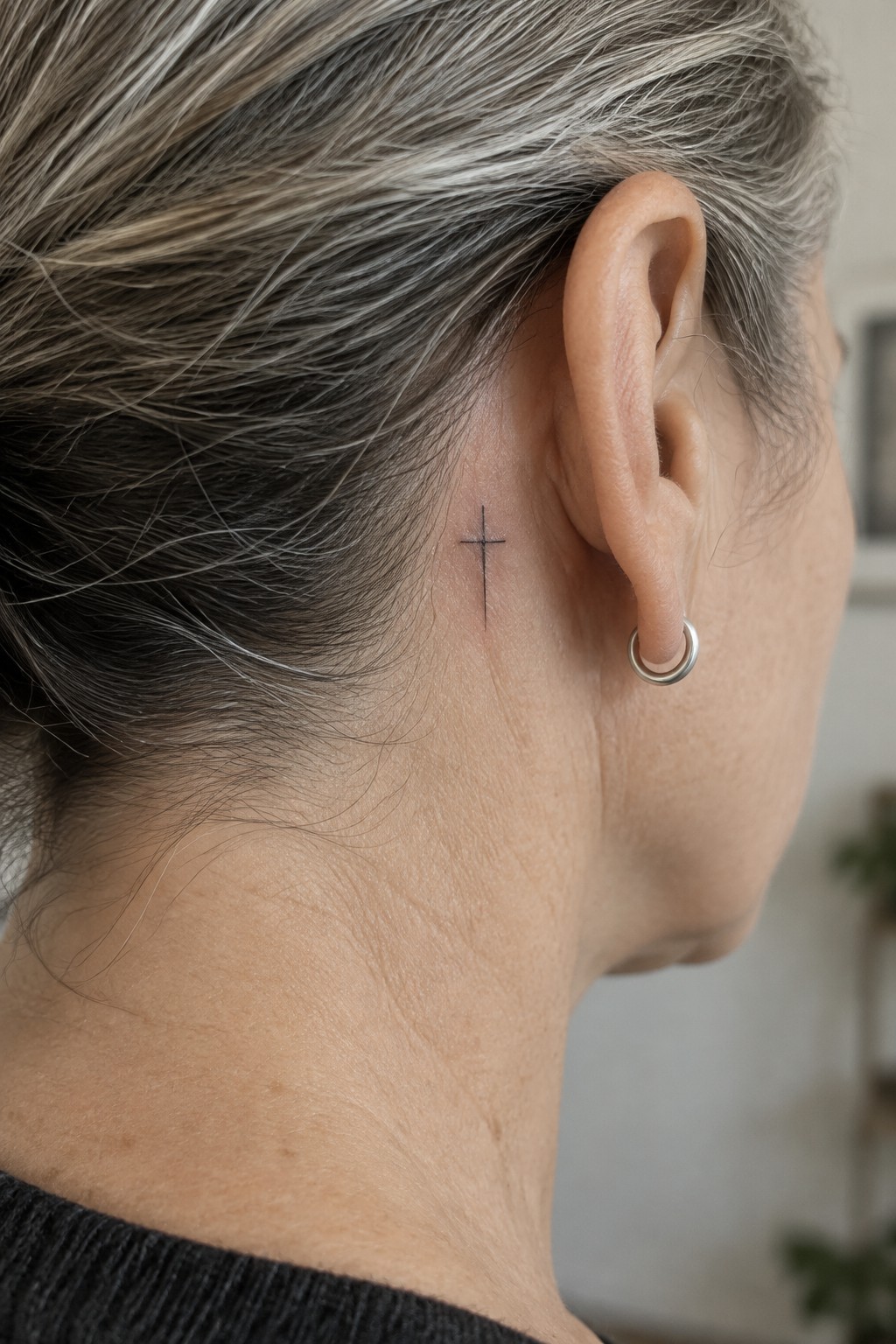 Graying hair pulled back, small cross tattoo behind ear with silver hoop earring