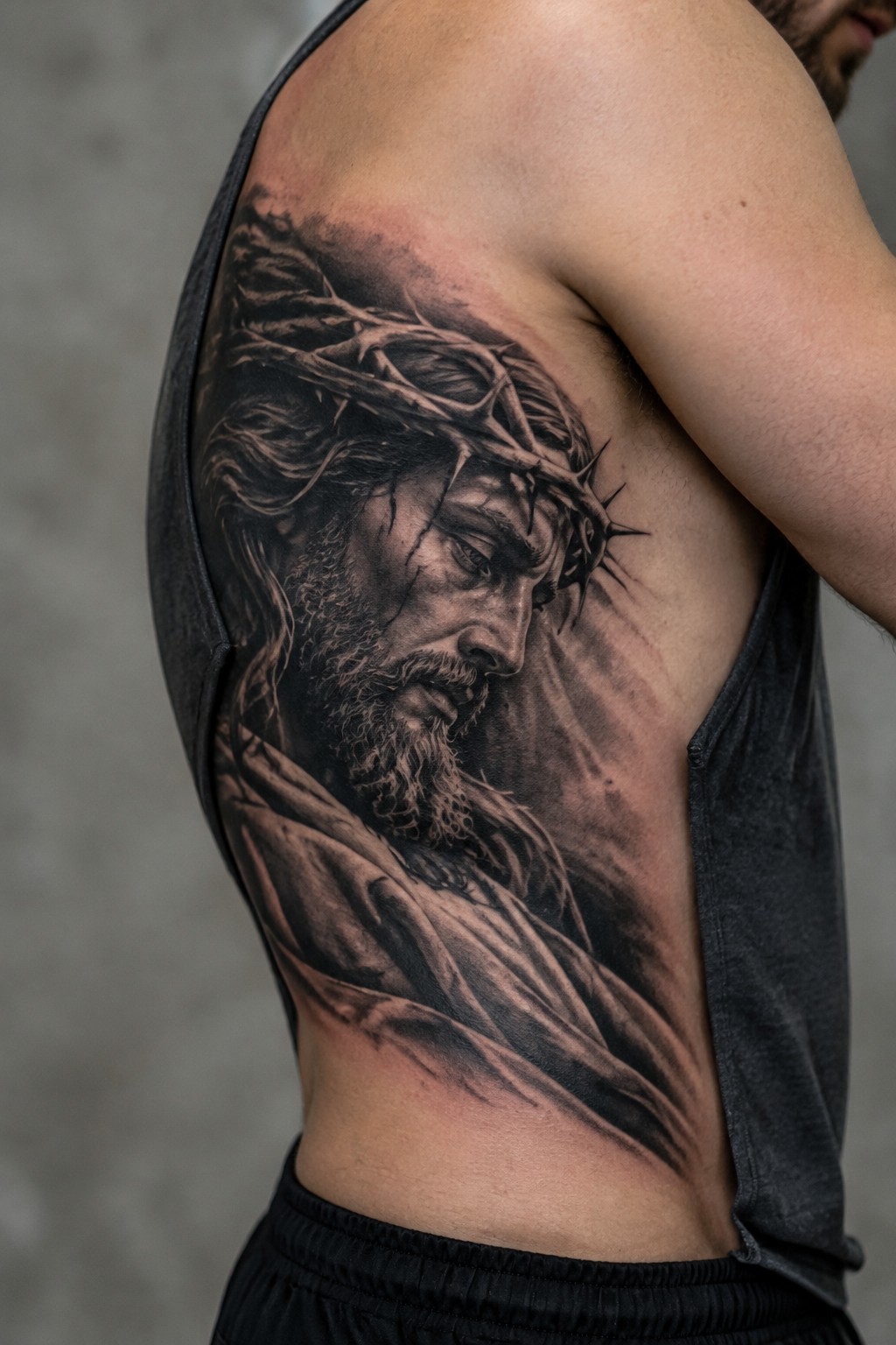 Realistic black and gray tattoo of Jesus with crown of thorns covering a man's upper arm and side torso