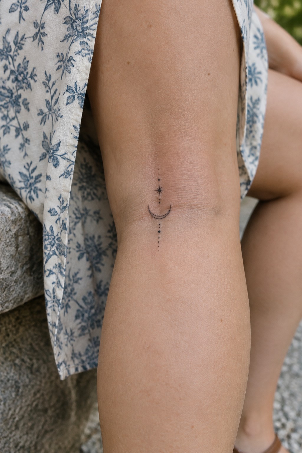 Fine line crescent moon, star, and dotted line tattoo centered on a woman’s knee.