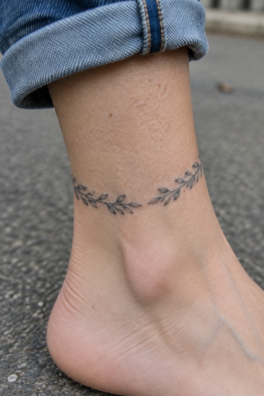 Fine line botanical garland tattoo wrapping around the ankle above the heel.