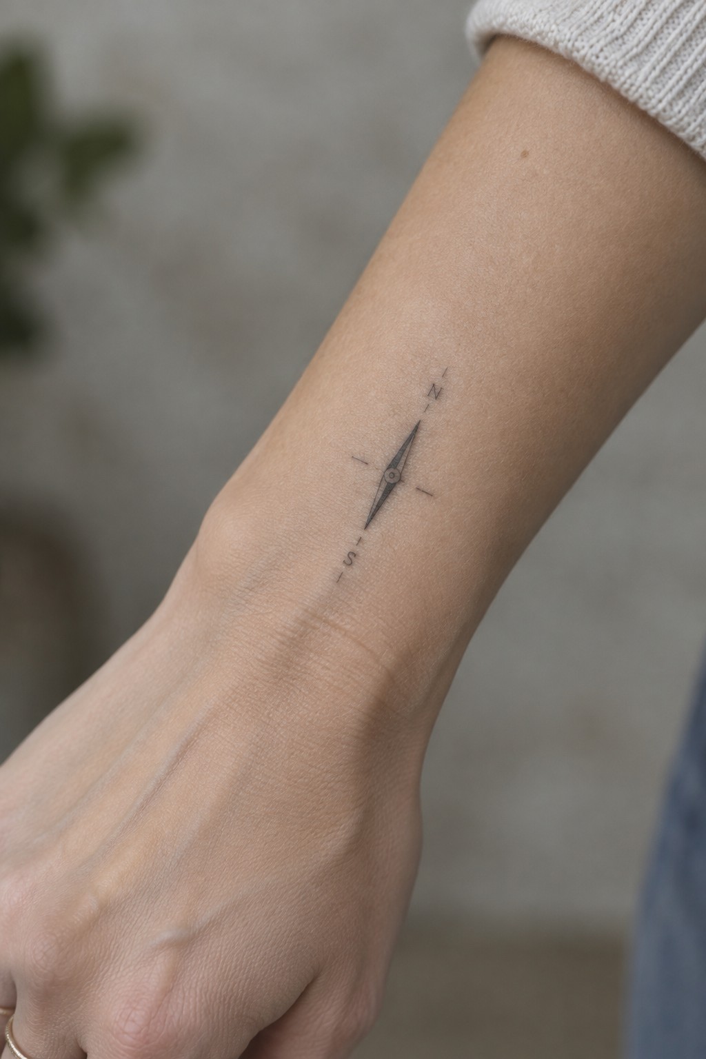 Small fine line compass tattoo with north and south markings on the inner wrist.