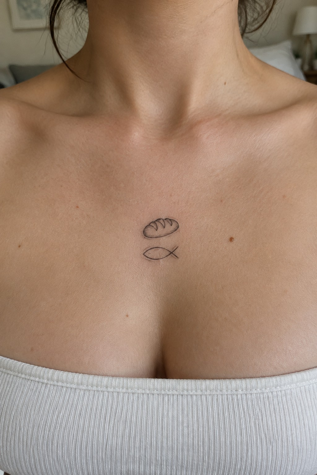 Small line drawing of a bread loaf above a fish symbol tattooed on the upper chest below the neck