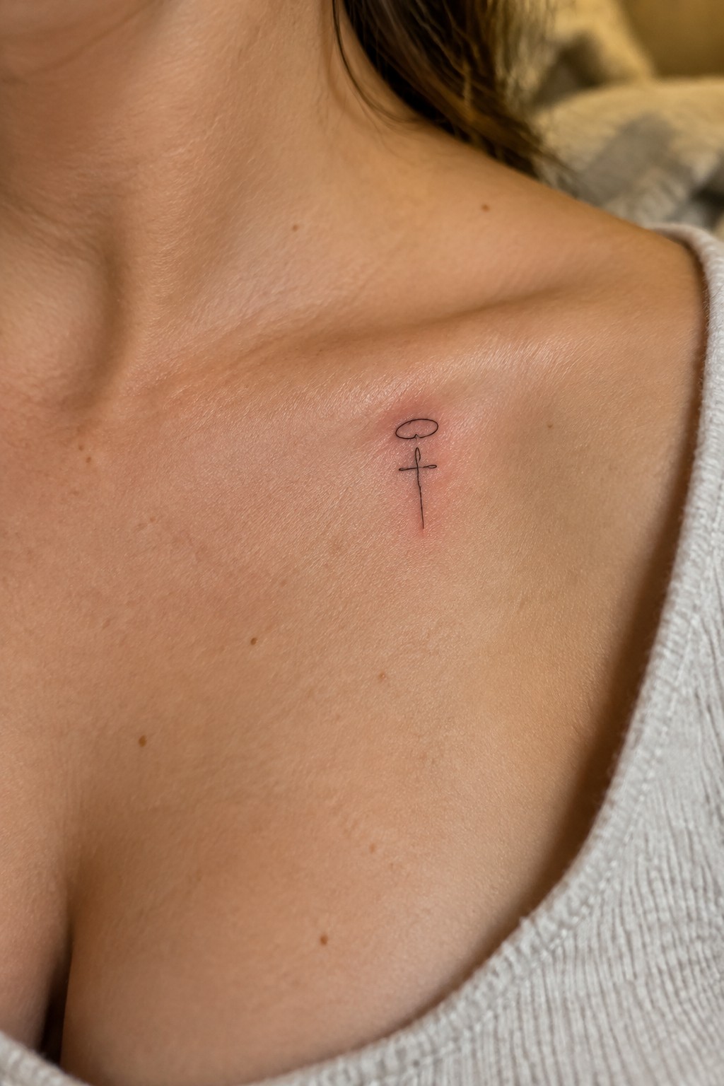 Small black cross tattoo with oval halo on upper chest, skin slightly red around it.