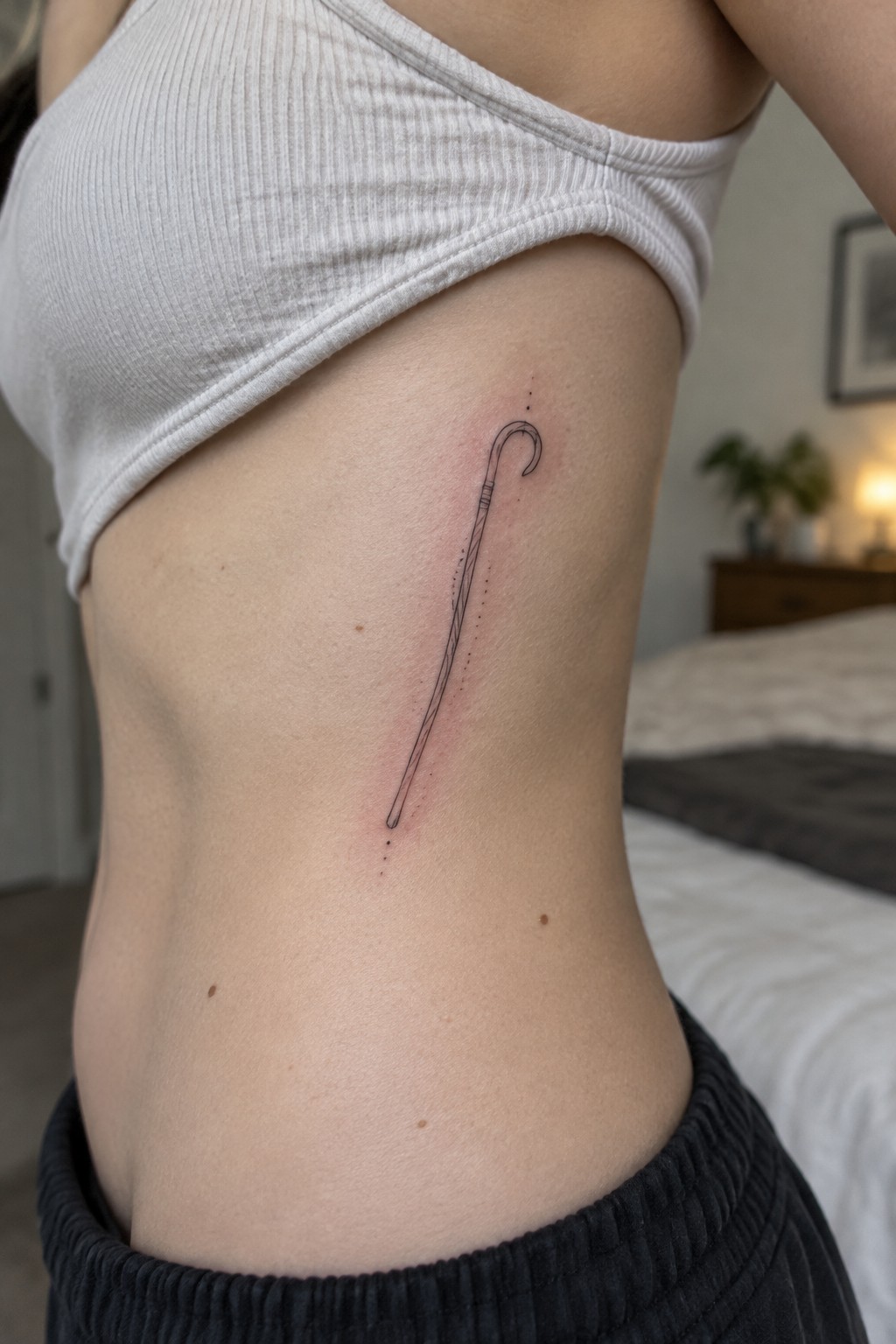 Fine line shepherd staff tattoo placed vertically on the side of the torso