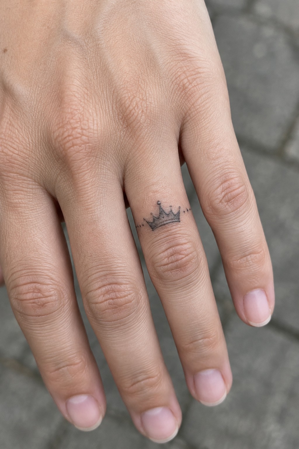 Light-skinned hand with small black crown tattoo and dots on ring finger.