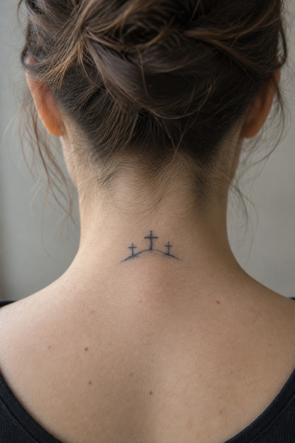 Three crosses tattoo on nape of neck below brown hair bun.