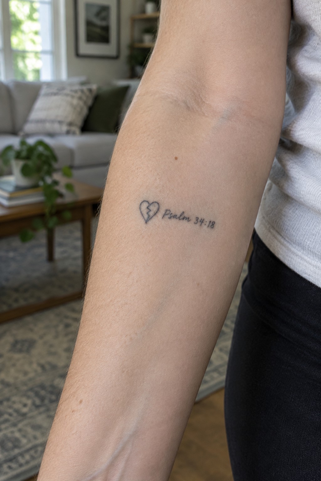 Broken heart tattoo with Psalm 34:18 on forearm in living room setting