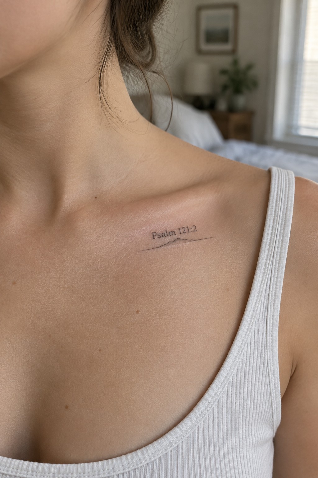 Collarbone tattoo reading Psalm 121:2 above mountain line on white tank top
