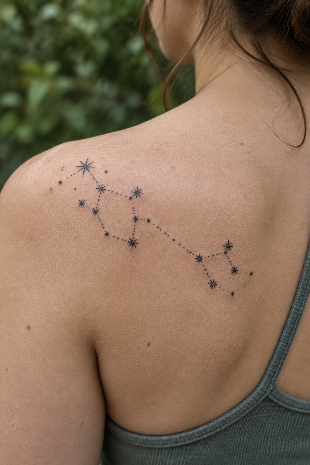 Fine-line constellation tattoo with dotted connections across a woman’s upper back and shoulder.