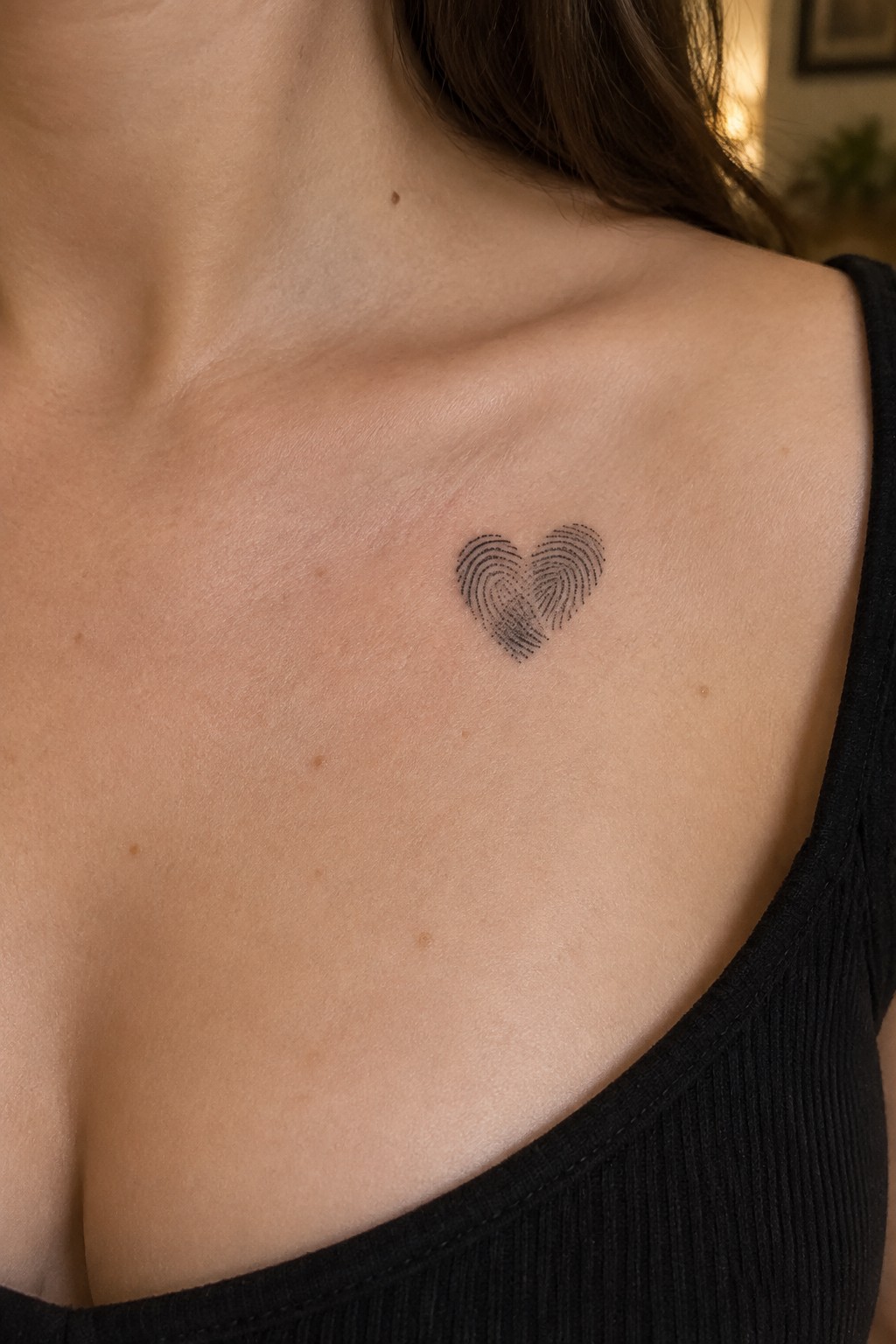 Small black fingerprint heart tattoo below a woman’s collarbone.