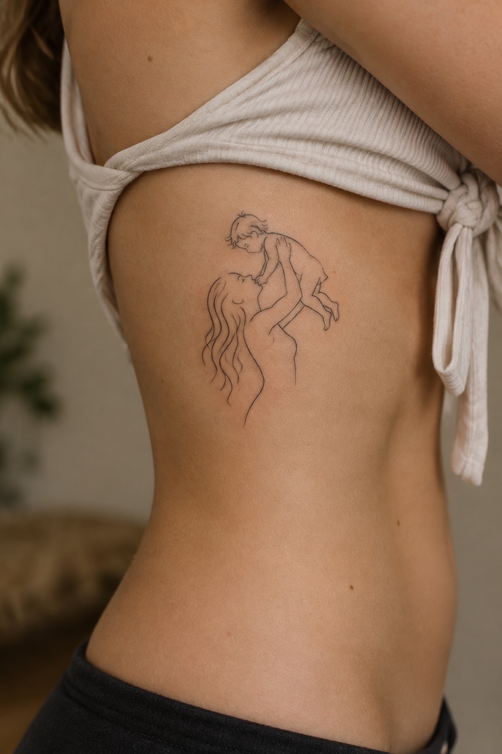 Fine-line tattoo of a mother lifting her child on a woman’s ribcage.