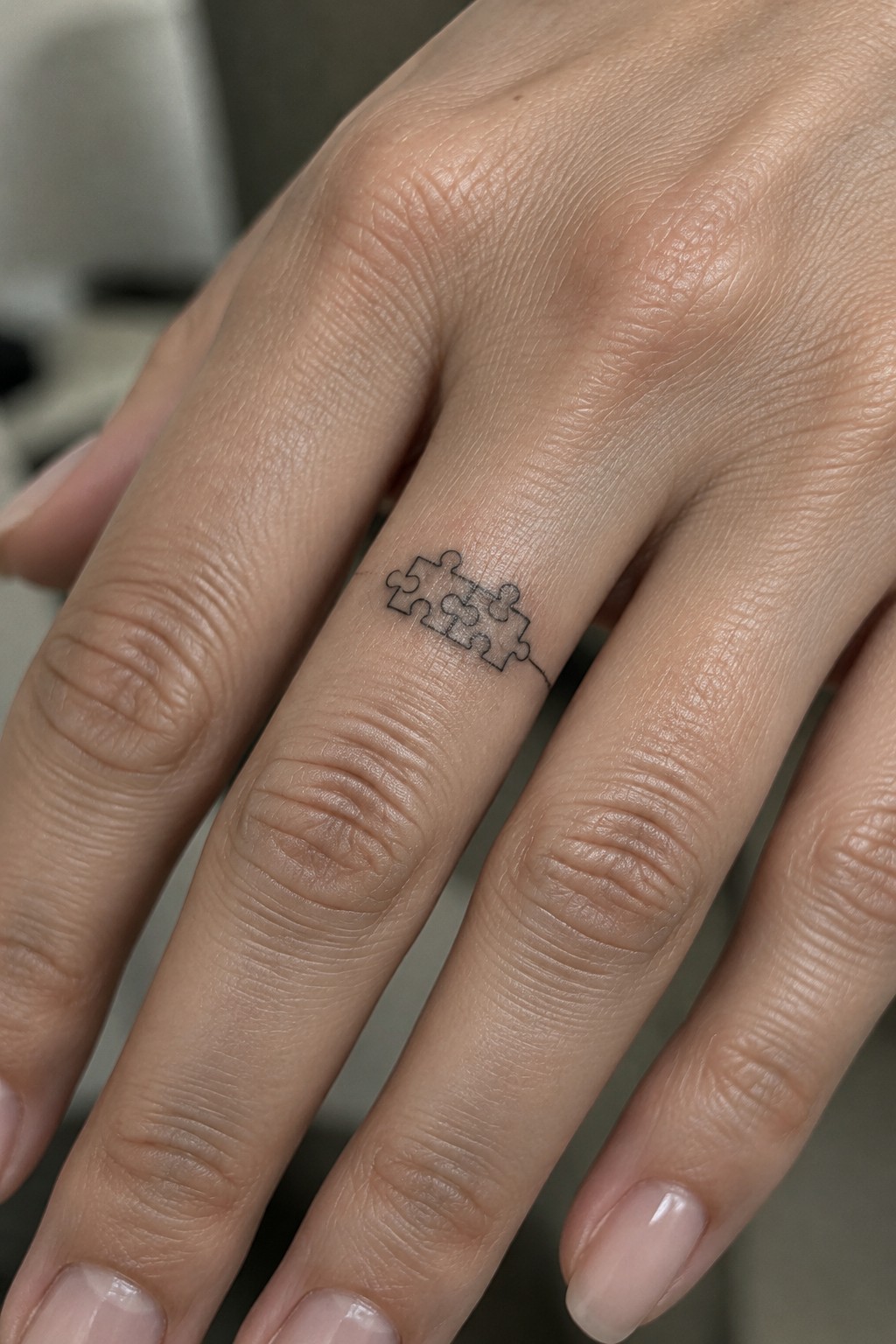 Small black outline tattoo of connected puzzle pieces on the side of a finger.