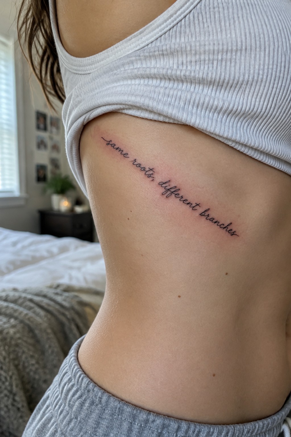 Fine script tattoo reading “same roots, different branches” along a woman’s side ribs.