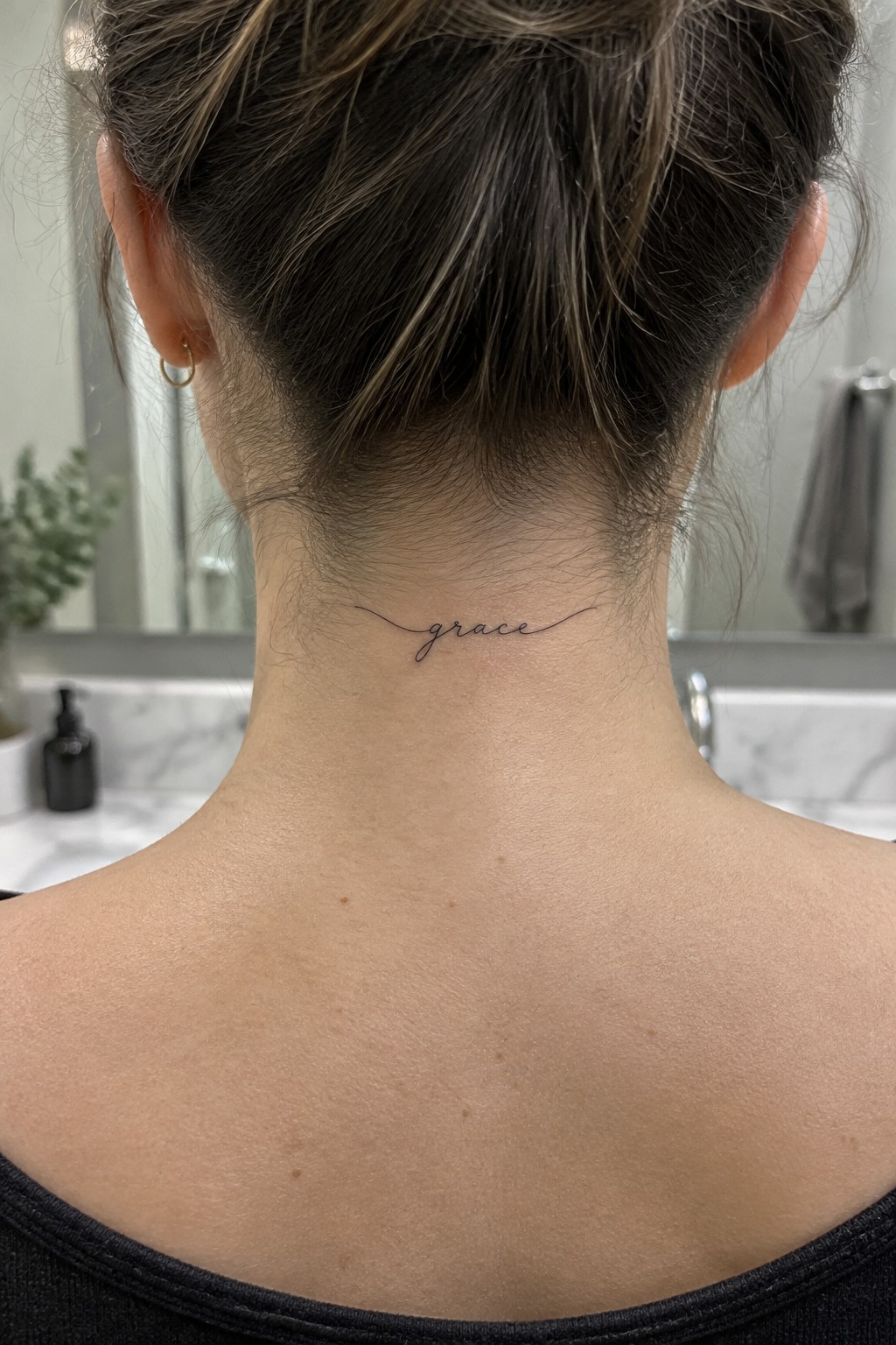 Small fine-line script tattoo reading “grace” at the nape, with thin lines extending on either side.