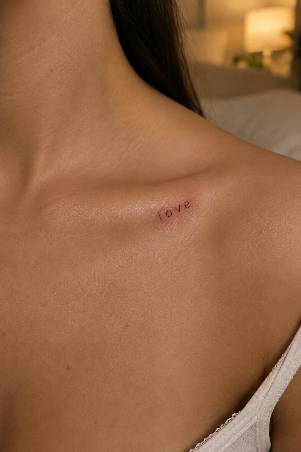 Small fine-line “love” tattoo below a woman’s collarbone.
